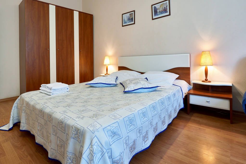 Una cama bien hecha con una colcha estampada, dos mesitas de noche con lámparas y un armario de madera.