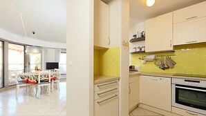 A modern kitchen with white cabinets, a yellow backsplash, and a dining area with a table and chairs. - Les allées du Cap by Interhome (Antibes)
