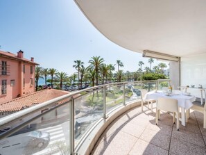 A balcony with a glass railing overlooking a street with parked cars and palm trees. - Les allées du Cap by Interhome (Antibes)