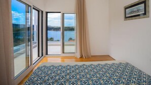 Et værelse med en stor skydedør, der fører ud til en balkon med udsigt over et sø og bakker.