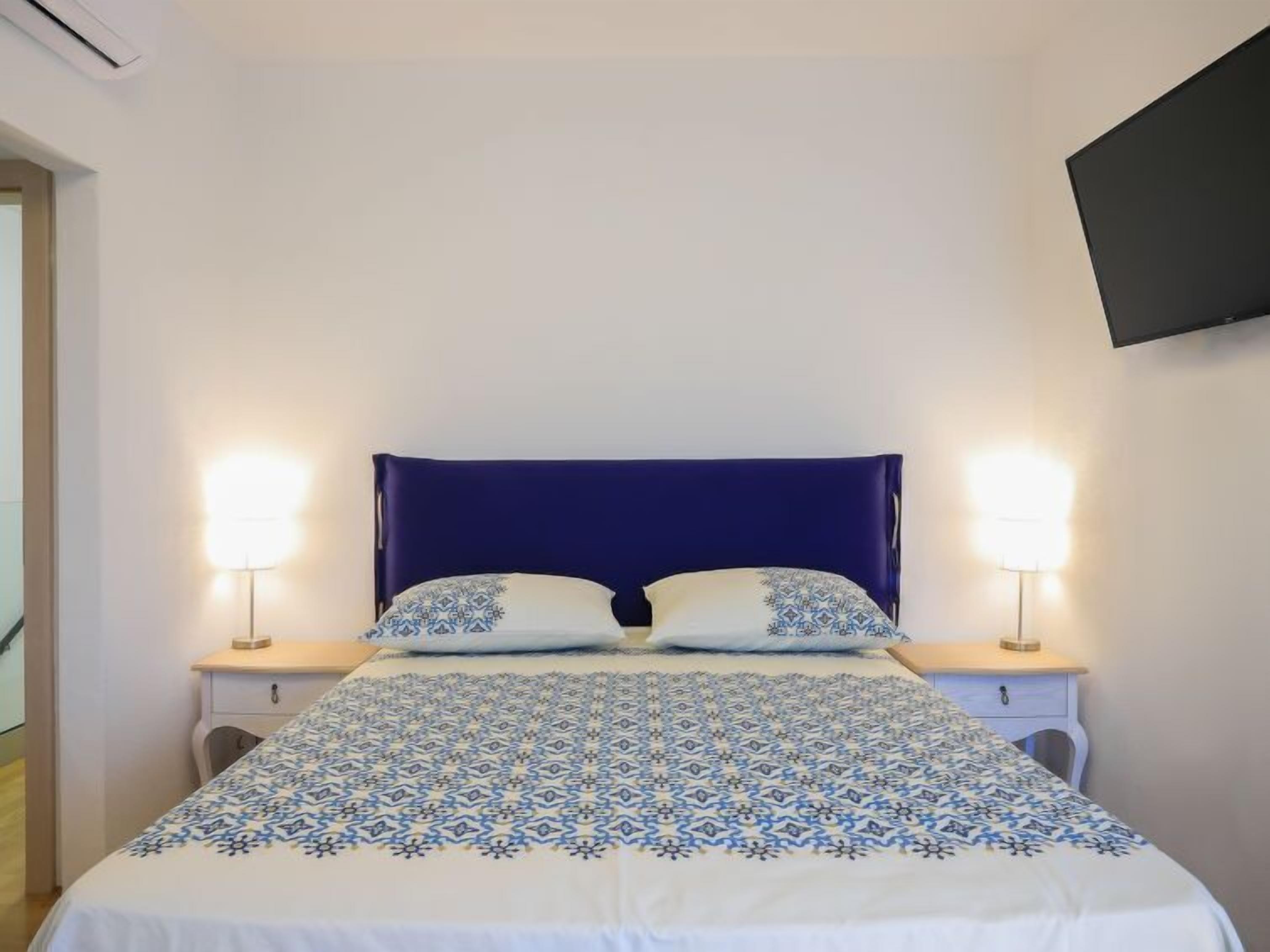 Un dormitorio con una cama grande, dos mesitas de noche y un televisor montado en la pared.