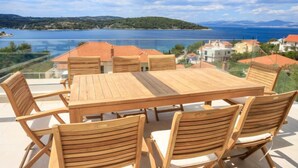 Et træbord og stole på en udendørs terrasse med udsigt over en sø og huse i baggrunden.