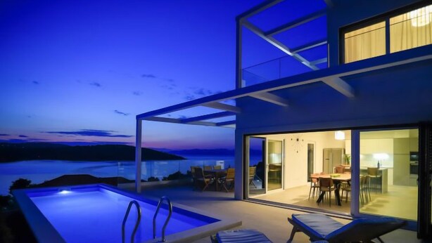 Et moderne hus med swimmingpool, liggestole og et spiseområde med udsigt over vandet.