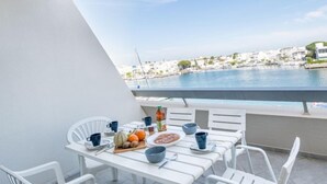 Un balcon avec une table dressée pour le petit-déjeuner, donnant sur une marina où l’on peut admirer des bateaux et des bâtiments.