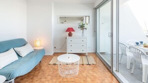 Un salon moderne avec un canapé bleu, une table ronde blanche et une commode blanche surmontée d’une lampe rouge.
