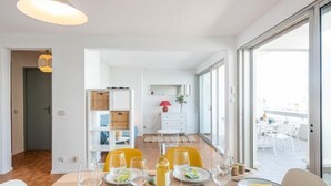 Un espace de repas moderne avec une table dressée pour quatre personnes, une bouteille de vin et une lampe rouge en arrière-plan.