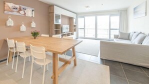 Ein modernes Wohnzimmer mit einem Holzesstisch, weißen Stühlen, einer Couch und einem großen Fenster mit Blick.