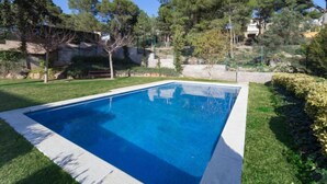 Una piscina rectangular con superficie de agua azul cristalina, rodeada por un césped cuidado y diversos árboles.
