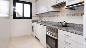 Una cocina moderna con armarios blancos, horno empotrado, lavadora y ventana.