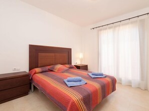 A hotel room with a bed, a nightstand, a lamp, and a window with curtains.