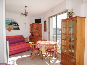 Une pièce comprenant un canapé, une table à manger avec des chaises, un buffet en bois et une grande fenêtre.