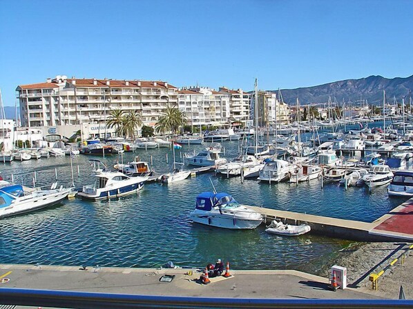 Un puerto deportivo con numerosas embarcaciones amarradas, un gran edificio de hotel al fondo y un cielo despejado.