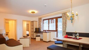 A compact living space with a sofa, a dining table, a bench, a TV, and a kitchenette.