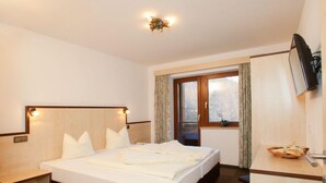 A hotel room with a large bed, bedside tables, a TV, and a window with curtains.