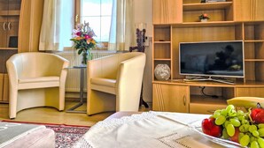 A well-lit room with two chairs, a TV, a bookshelf, and a window with curtains. - Lueg ins Land by Interhome (Reith bei Seefeld)