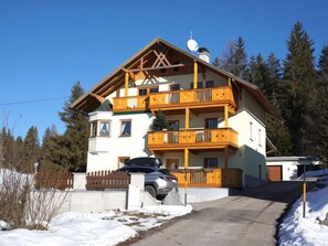 Una chalet a più piani con balconi in legno, un'antenna parabolica e un'auto parcheggiata davanti.
