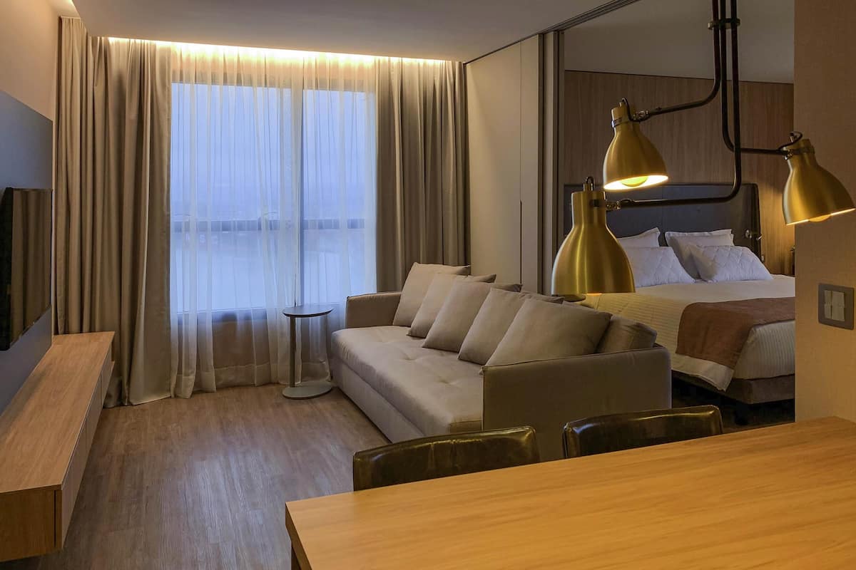 A hotel room with a sofa, a bed, a desk, and a lamp.