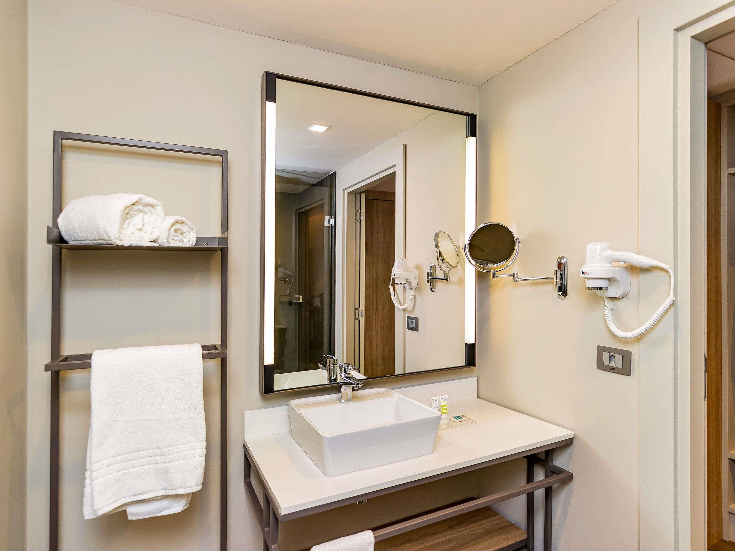 Un baño con un espejo grande, un lavabo, un perchero para toallas y un secador de pelo.