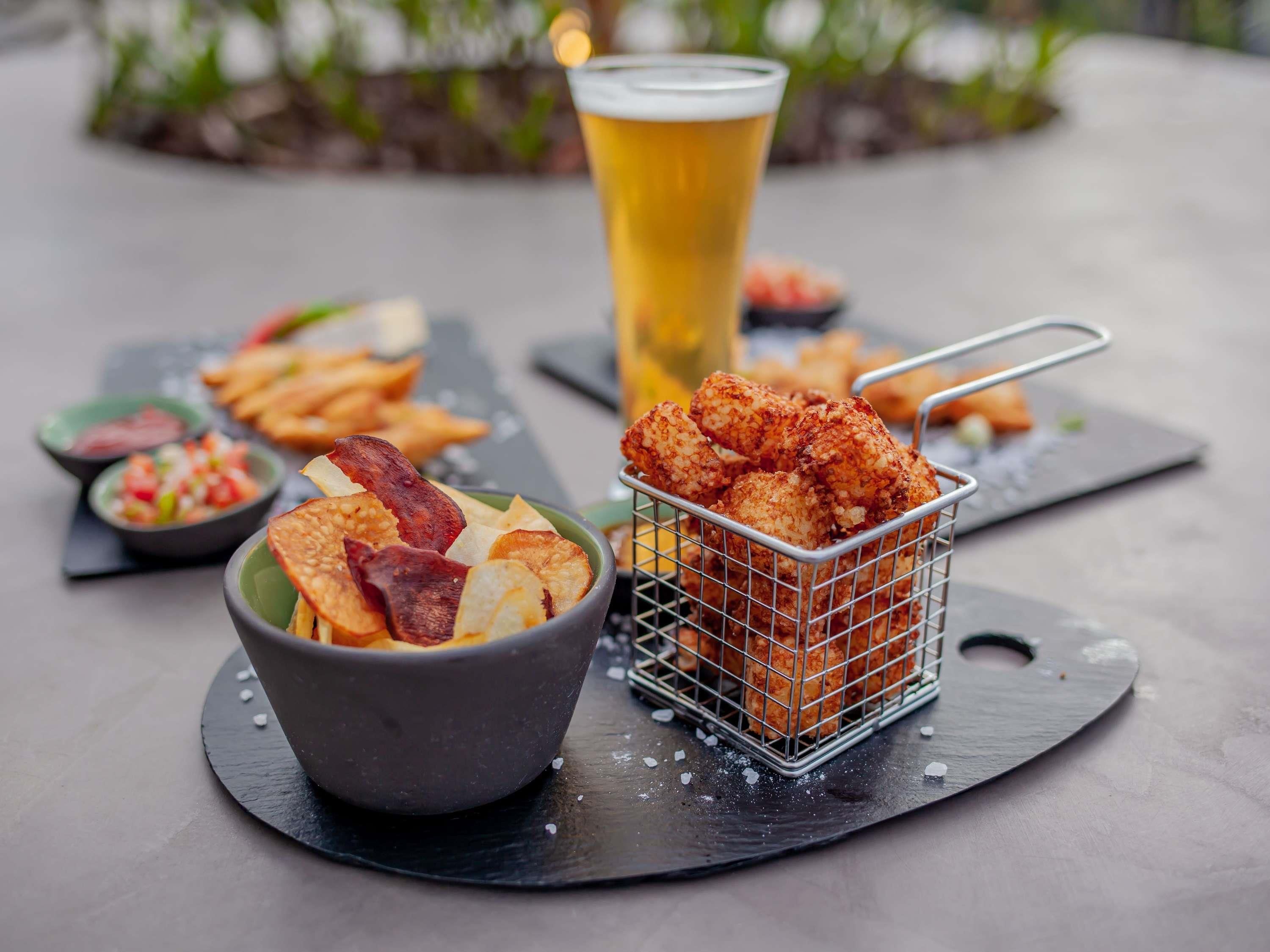 Un repas composé d’ailes de poulet frites, d’une bière et de divers accompagnements, le tout servi sur une planche en ardoise.