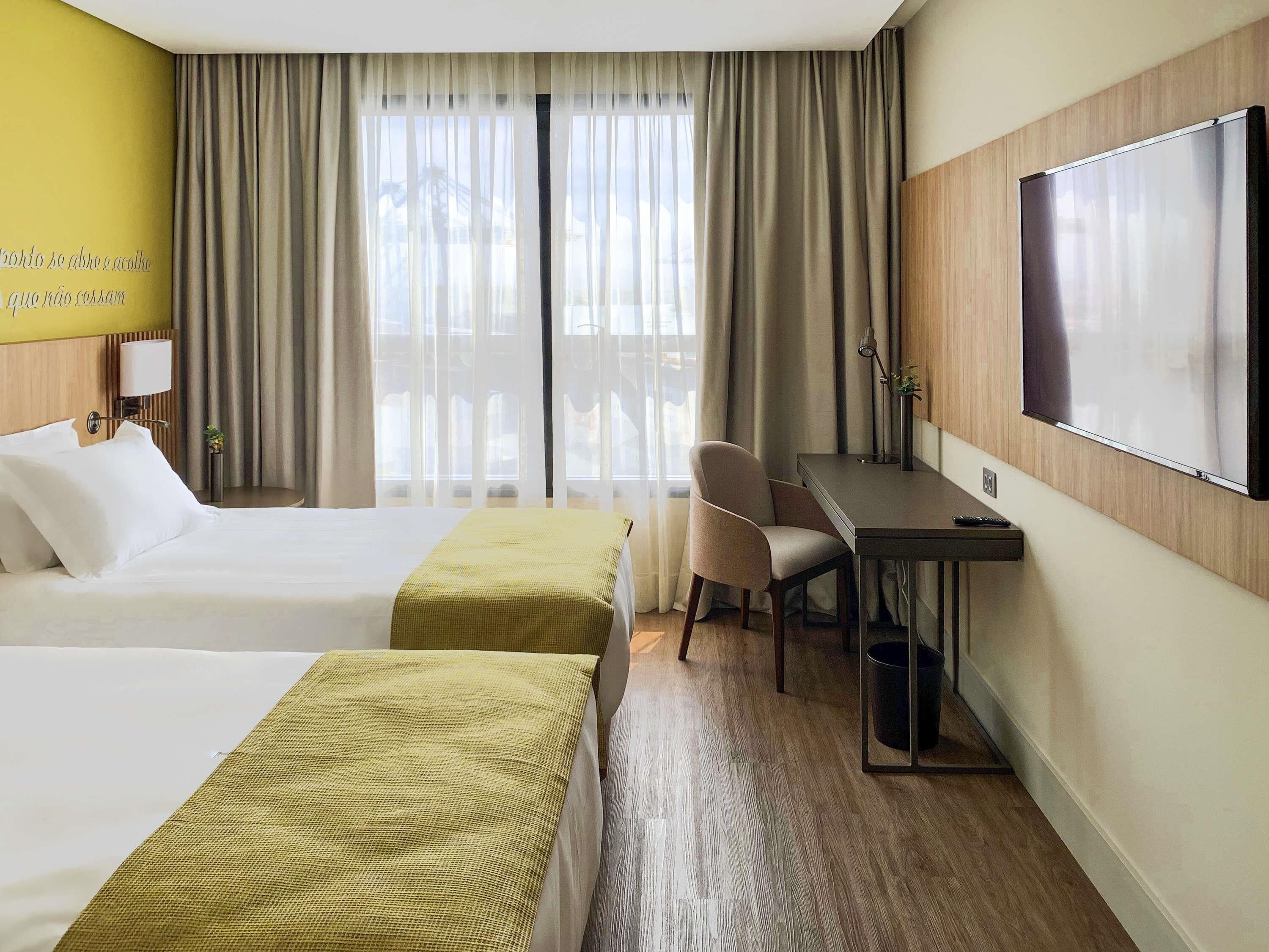 Habitación de hotel con dos camas, un escritorio, una silla, un televisor y una ventana con cortinas.