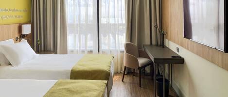 Habitación de hotel con dos camas, un escritorio, una silla, un televisor y una ventana con cortinas.