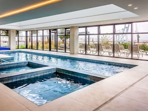 Une piscine intérieure offrant une vue dégagée sur la ville grâce à de grandes fenêtres.