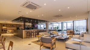 Un moderno vestíbulo de hotel con zona de bar, áreas de descanso y grandes ventanales con vistas.
