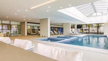 Una piscina interior con sillas de descanso, techo de vidrio y vistas al exterior.