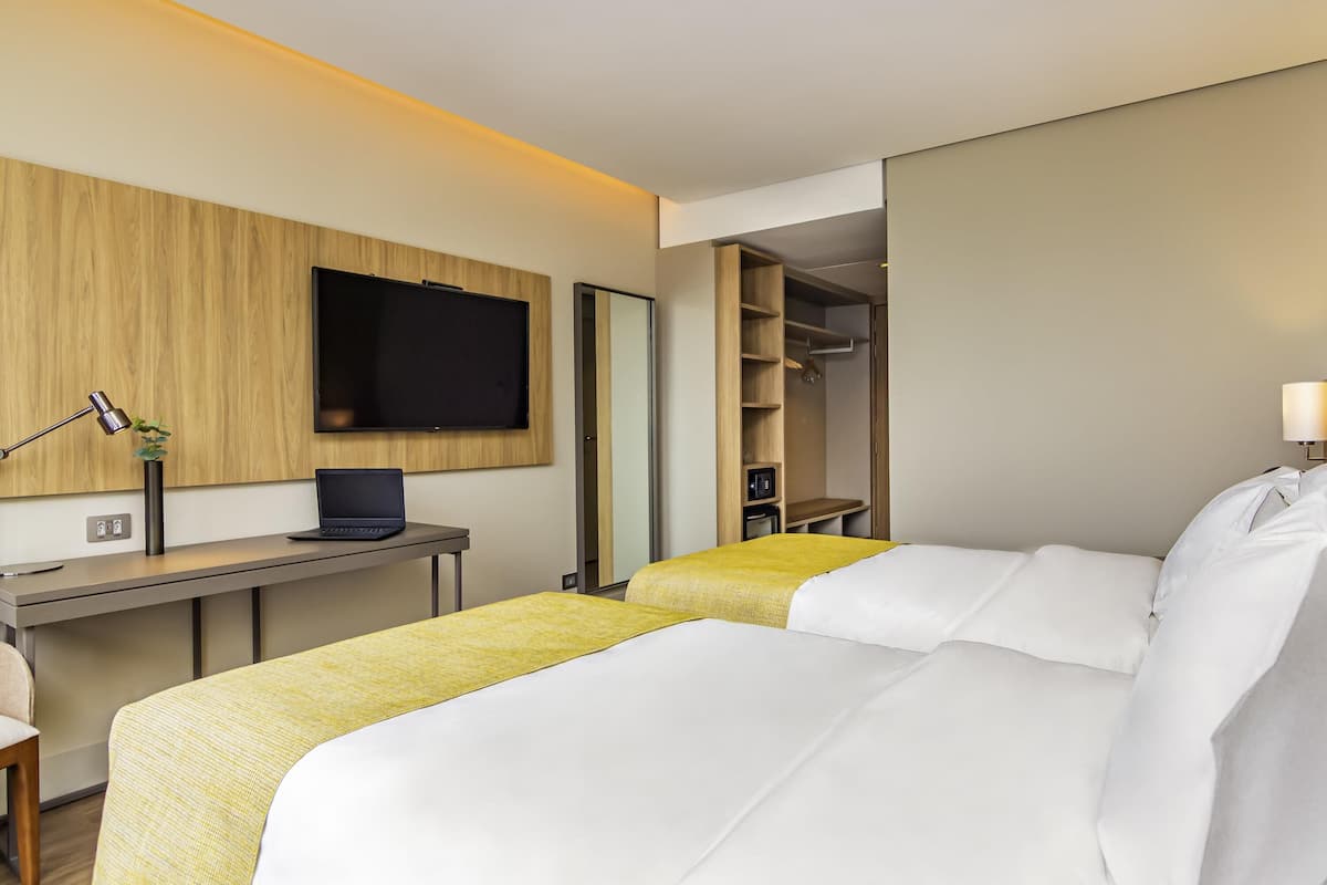 A hotel room with a bed, a desk with a laptop, a TV, and a wardrobe.