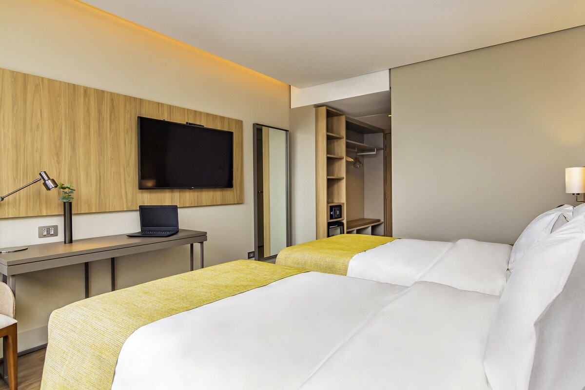 Une chambre d’hôtel équipée d’un lit, d’un bureau avec un ordinateur portable, d’une télévision et d’une armoire.