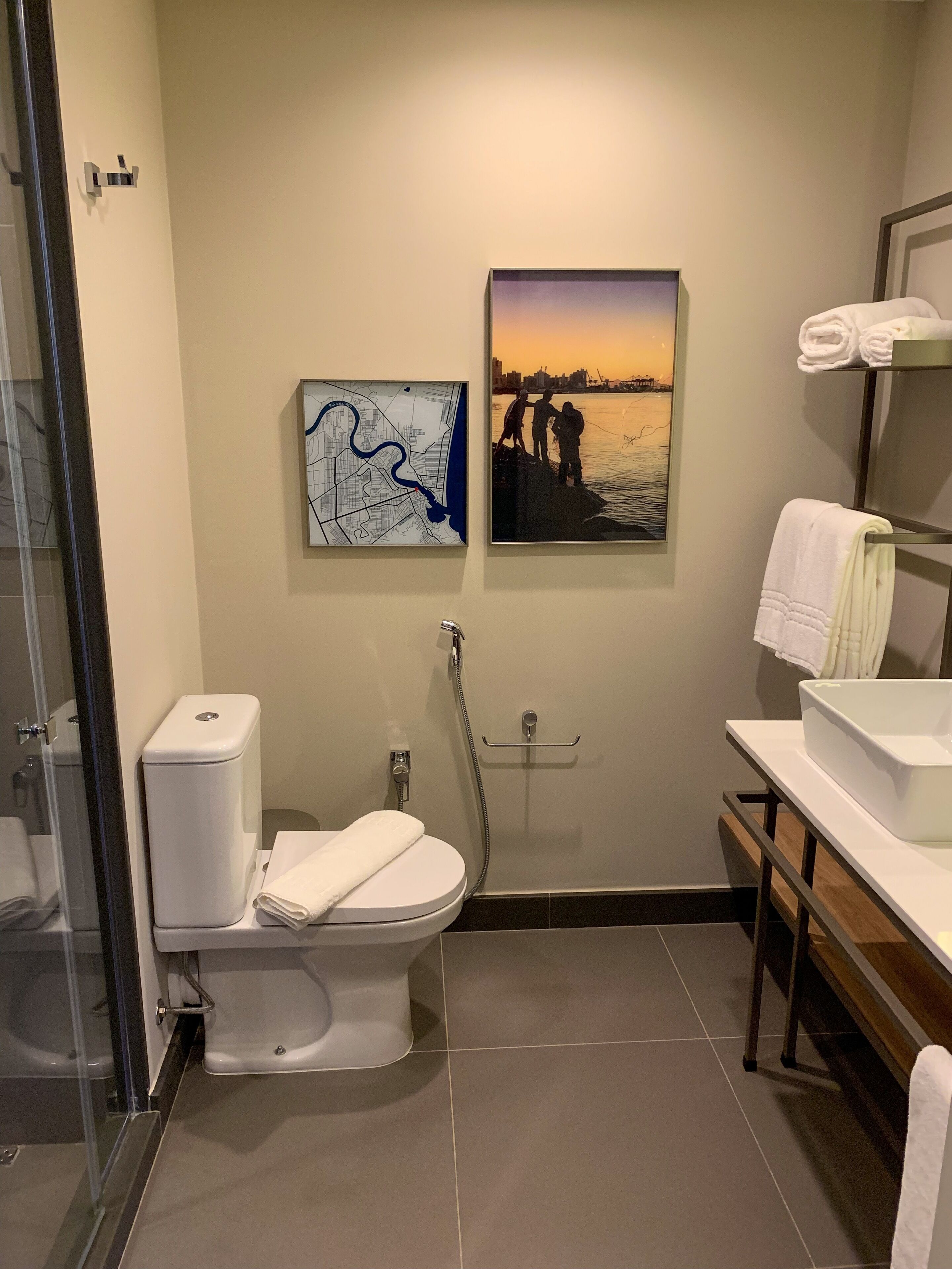 Ein modernes Badezimmer mit Toilette, Bidet und Dusche. An der Wand hängen zwei Bilder: eine Karte und eine Sonnenlandschaft.