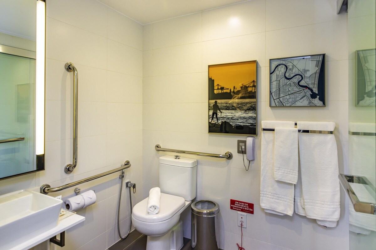 Une salle de bain moderne équipée de toilettes, d’un bidet, de barres d’appui, d’un lavabo et d’une poubelle.