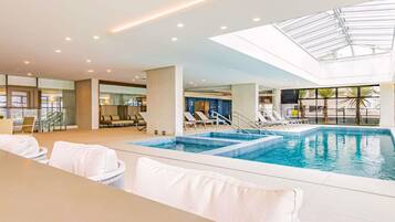 A swimming pool with sun loungers, a glass ceiling, and a view of the outside.