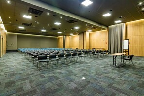 Un salón de conferencias con filas de sillas, una pizarra y una mesa.