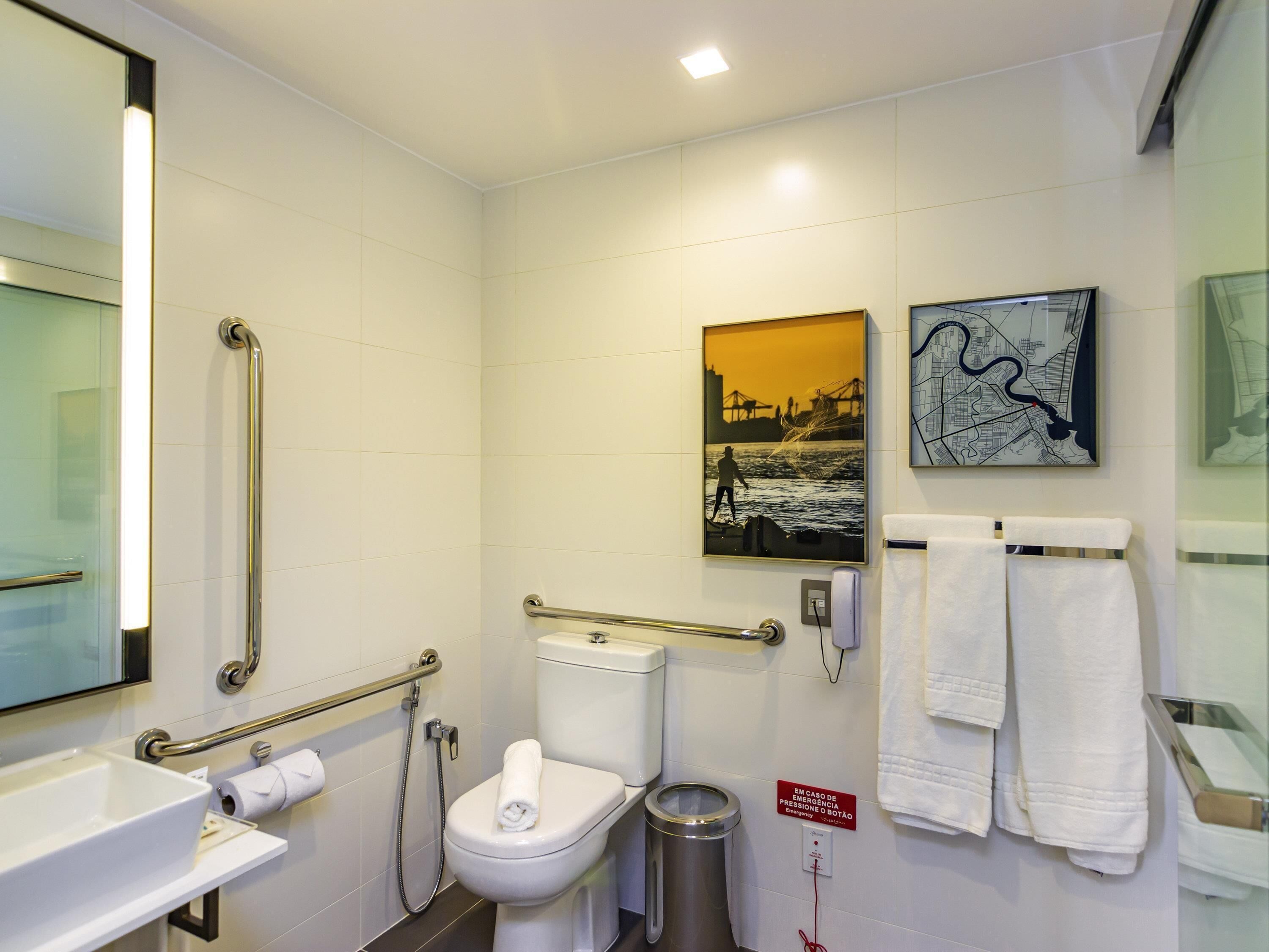 Een moderne badkamer met toilet, hygiëneslot, handgrepen, wastafel en prullenbak.