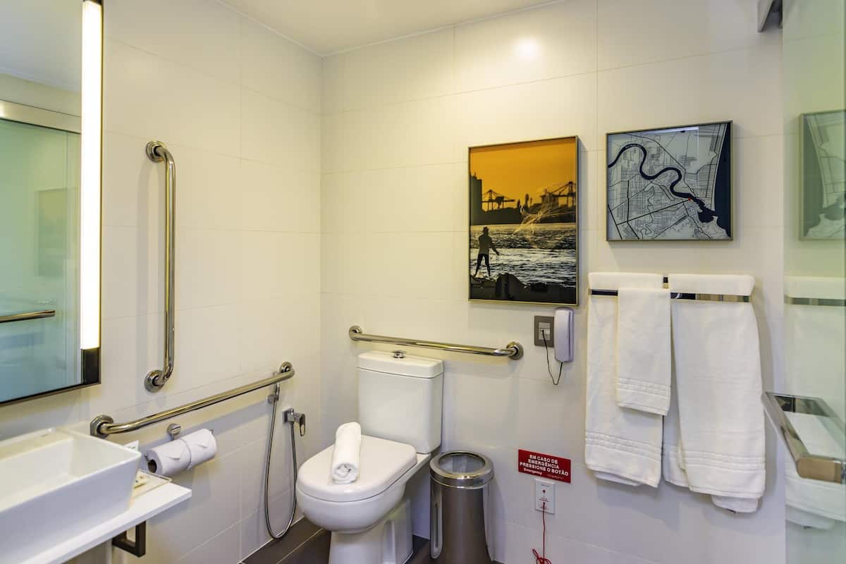 A modern bathroom with a toilet, bidet, handrails, a sink, and a trash can.