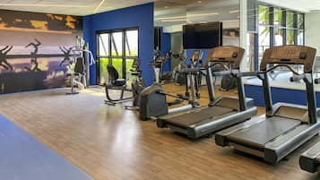 Een sportschool met loopbanden, elliptische trainers en een grote spiegel.