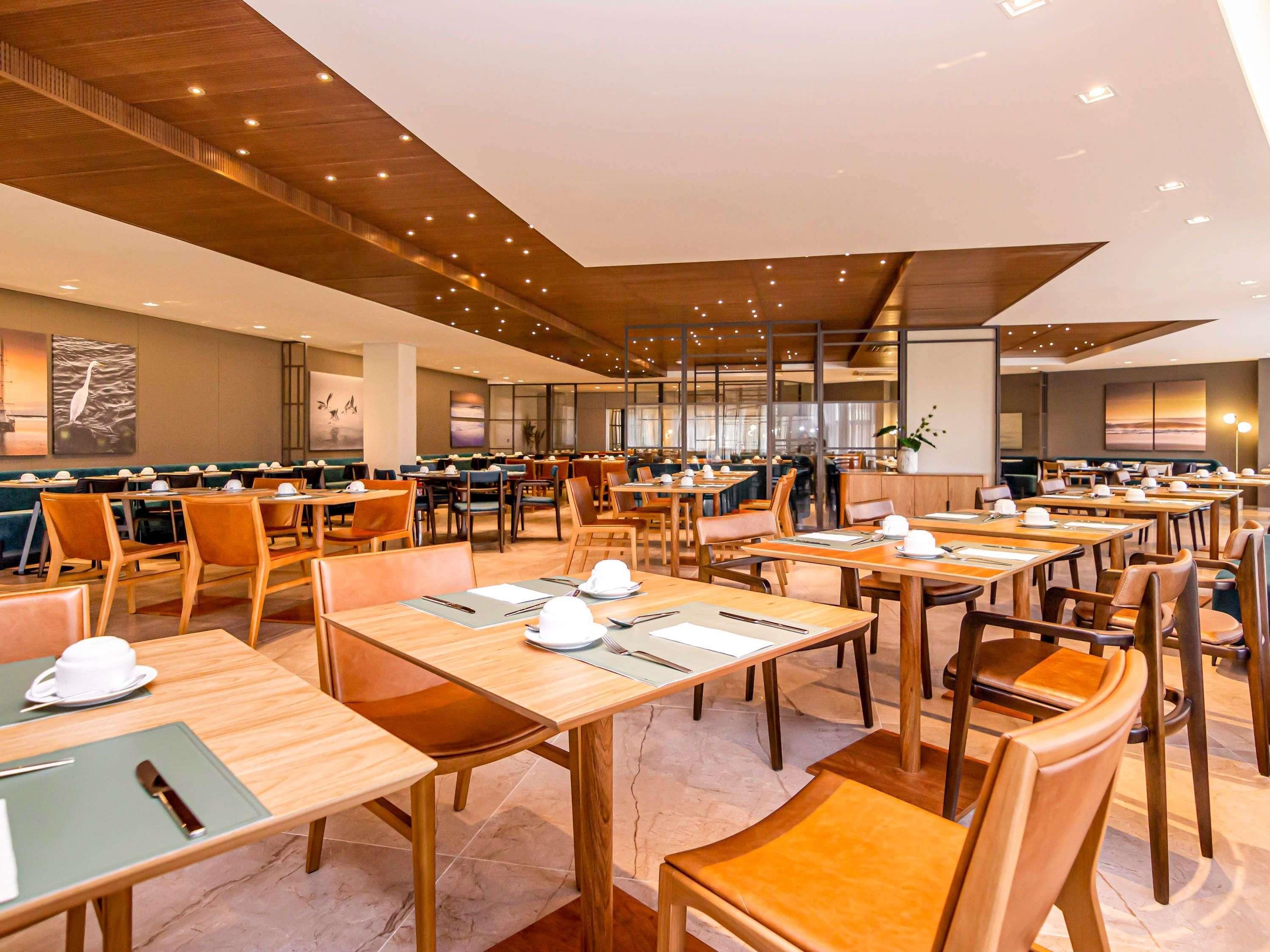 A spacious dining area with multiple tables and chairs, a high ceiling with wooden beams, and large windows.