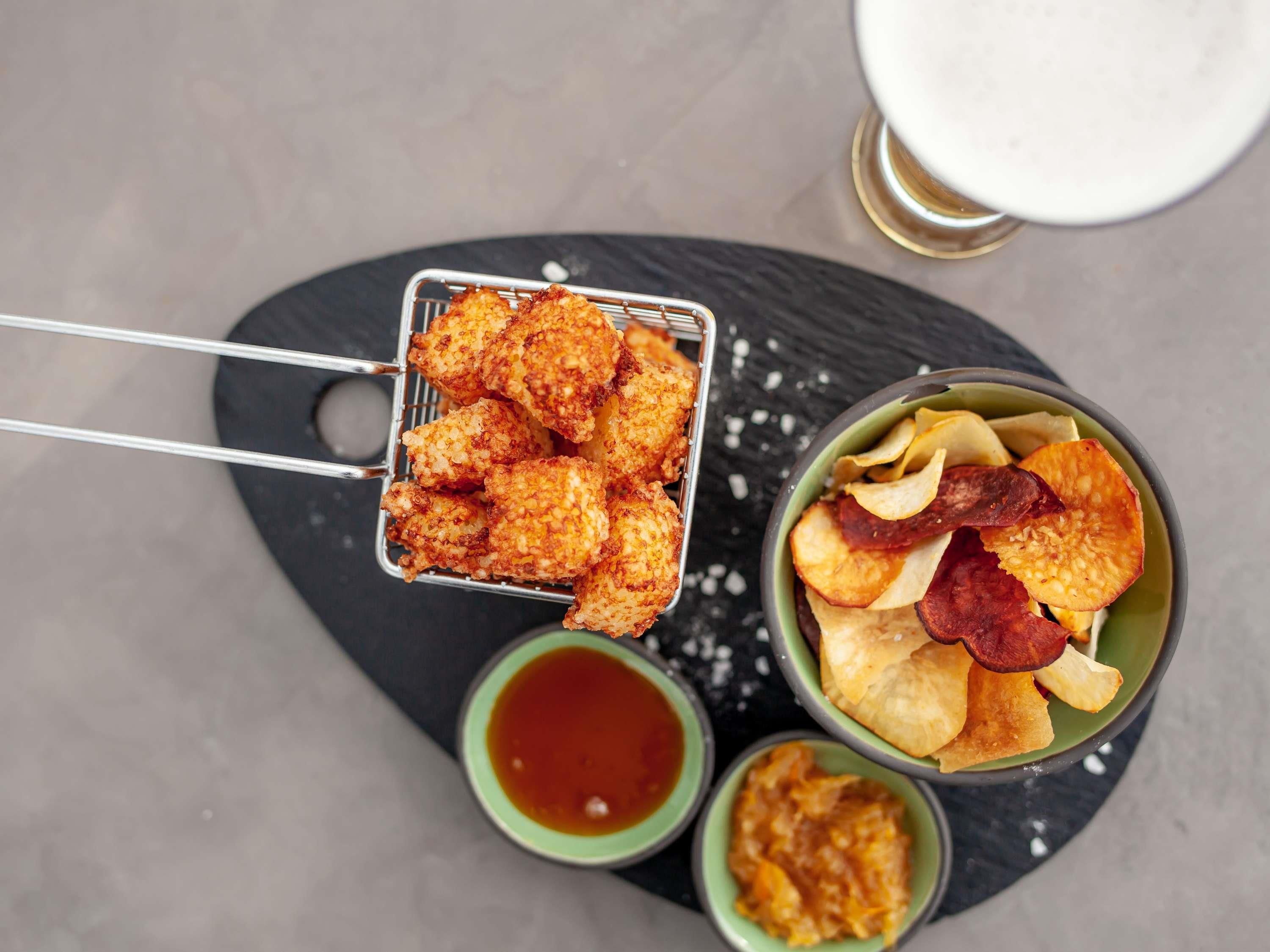 Een schaal met gebakken snacks, een kom chips met lekkernijen en een klein schaaltje saus.