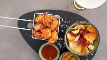A tray of fried food items, a bowl of chips with snacks, and a small bowl of sauce.