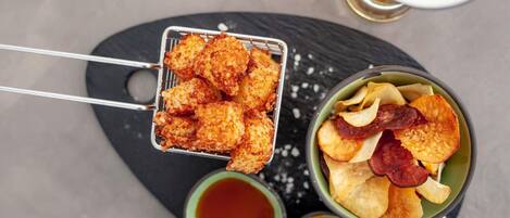 A tray of fried food items, a bowl of chips with snacks, and a small bowl of sauce.
