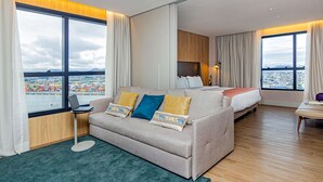 Een moderne hotelkamer met een groot bed, een bank, een bureau en uitzicht op een stadsbeeld.