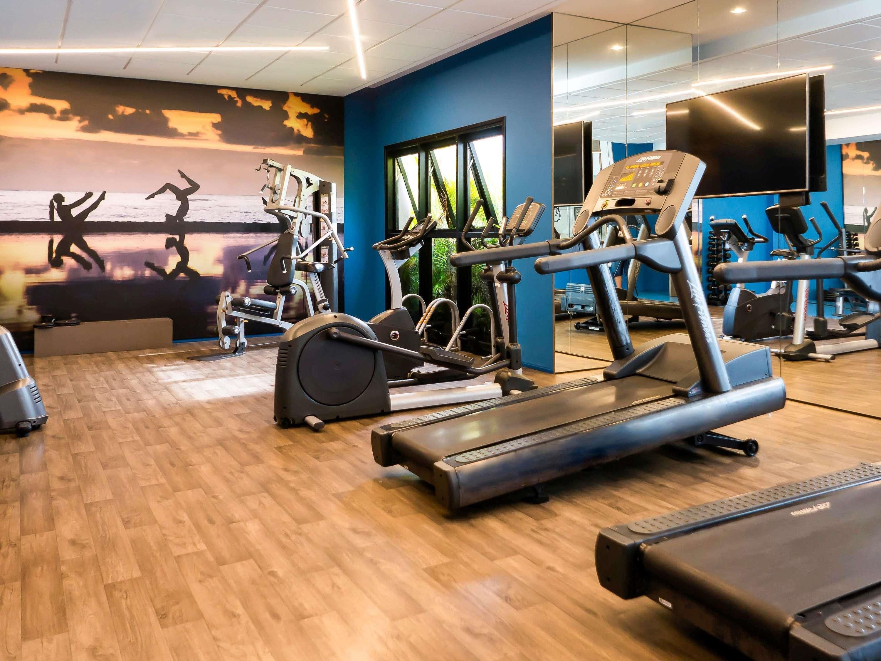Een sportschool met trainingsapparatuur, een grote spiegel en een muurschildering.