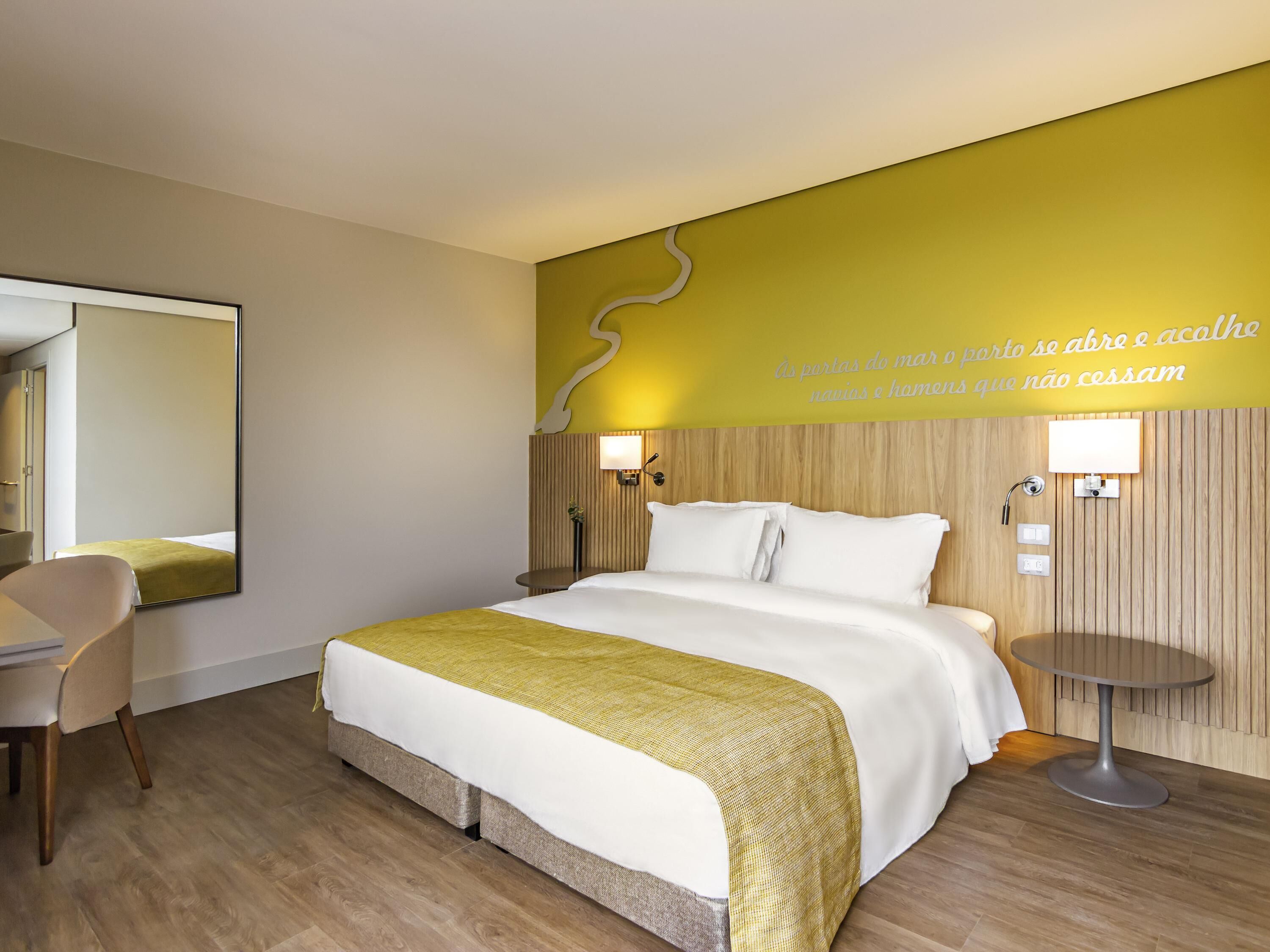 Une chambre d’hôtel avec un lit, une table de chevet, une chaise et un miroir.