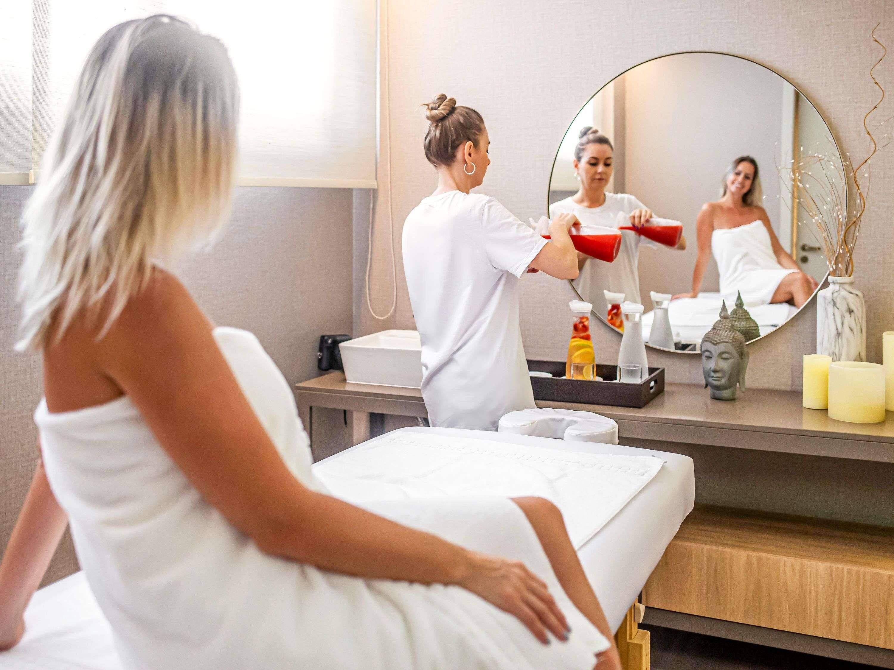 A hotel room with a bed, a mirror, a small Buddha statue, candles, and toiletries on a tray.