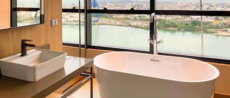 A modern bathroom with a freestanding bathtub, a sink, and a large window offering a view of a cityscape and a river.