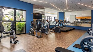 Een sportschool met trainingsapparatuur, grote ramen en een blauwe muur.
