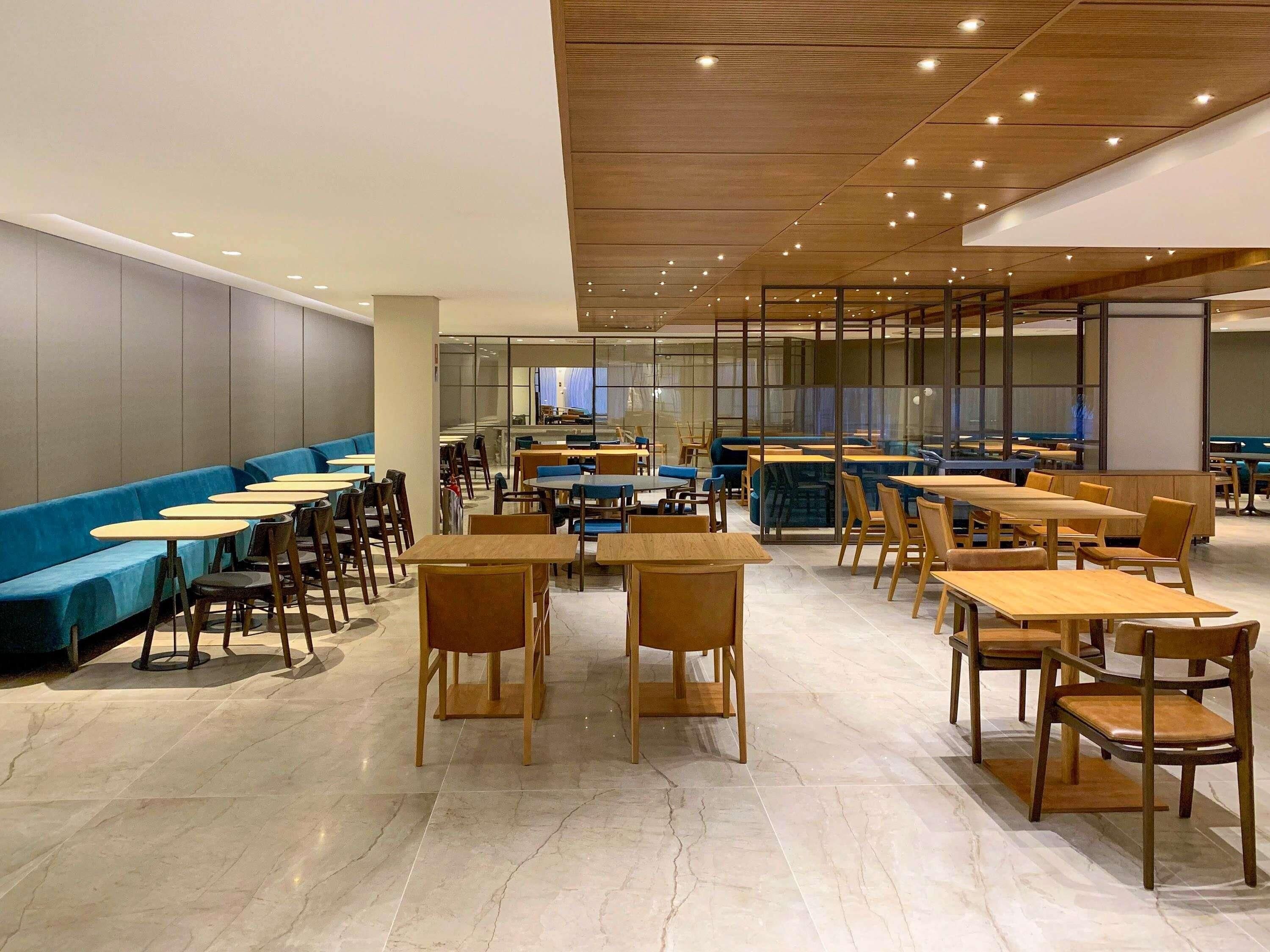 Un vaste espace intérieur aménagé pour les repas, avec de nombreuses tables et chaises, un canapé bleu et un design de plafond moderne.