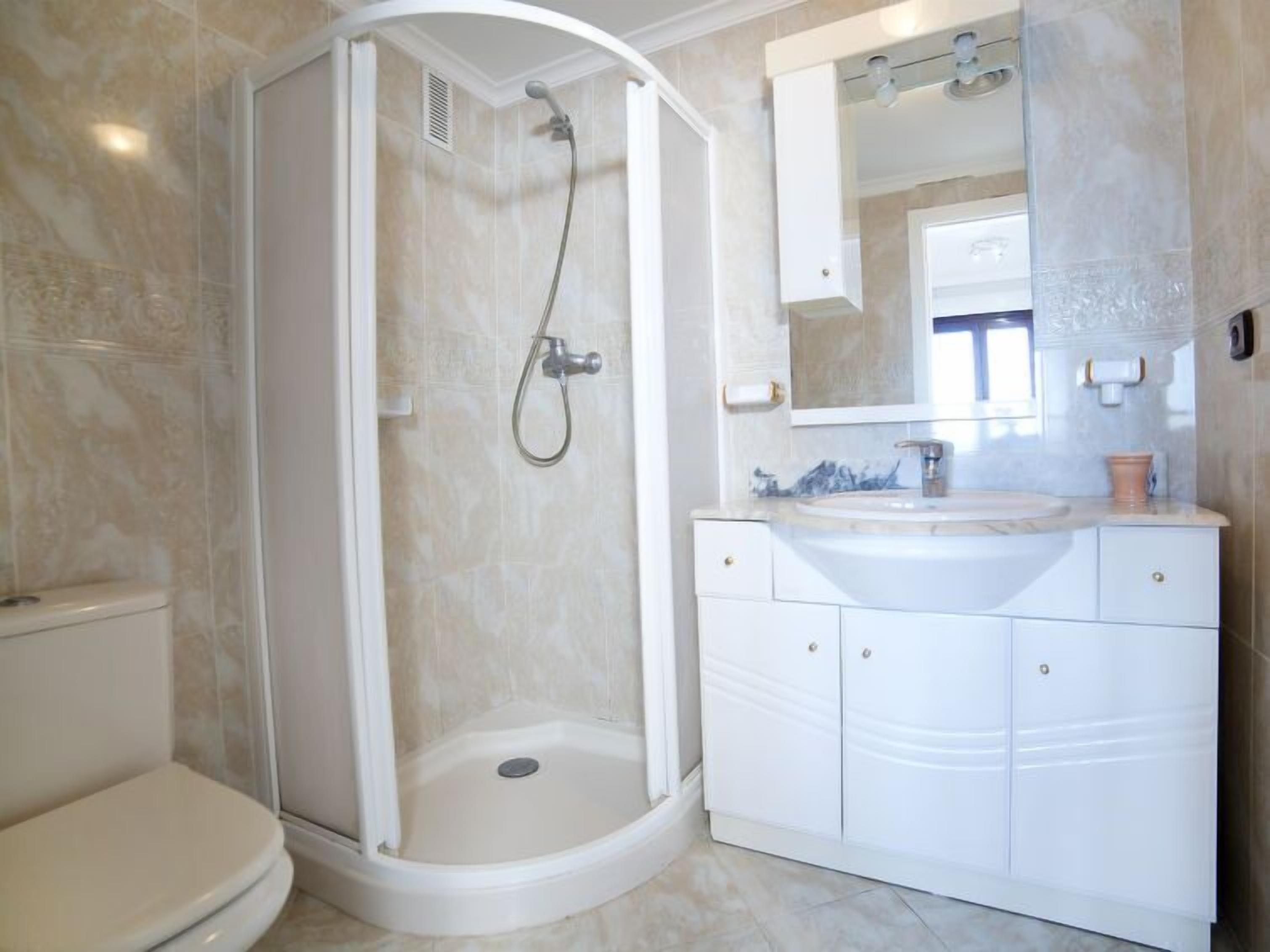 Une salle de bain avec une douche à l’italienne, des toilettes, un lavabo avec un miroir et des placards.