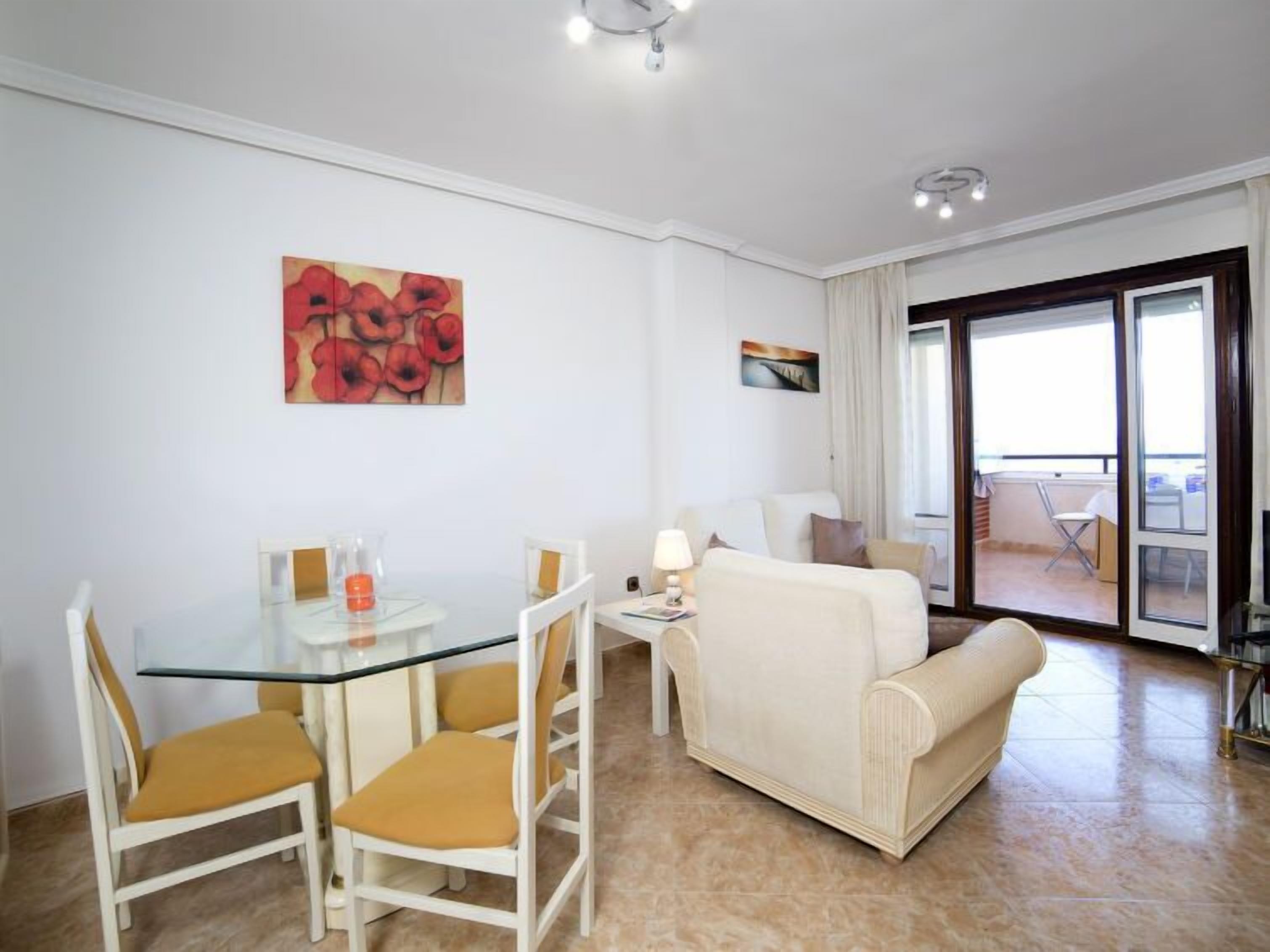 A modern living room with a glass dining table, white sofas, and a large window.